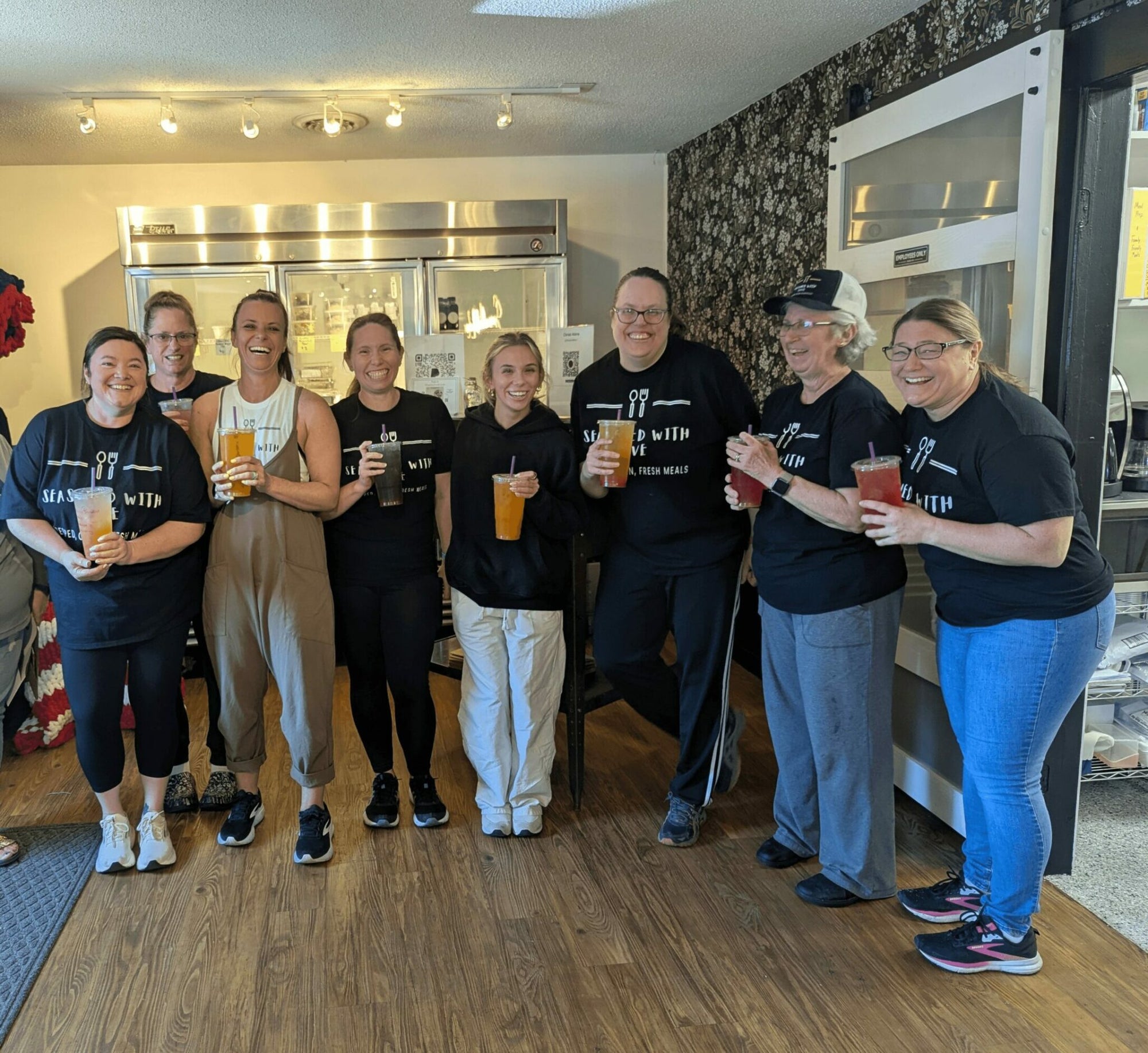 Group of people in a kitchen holding drinks and smiling
